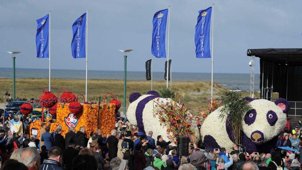 Giant panda-shaped Flower Parade floats and crowds at the Noordwijk Beach grandstand, with the North Sea behind